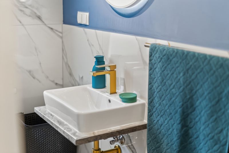 Top 5: bathroom with marble-look tiles, white basin, gold tap and a teal towel