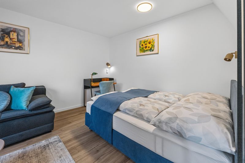 Top 5: double bed with blue bedding, a desk with a green lamp and a sunflower painting
