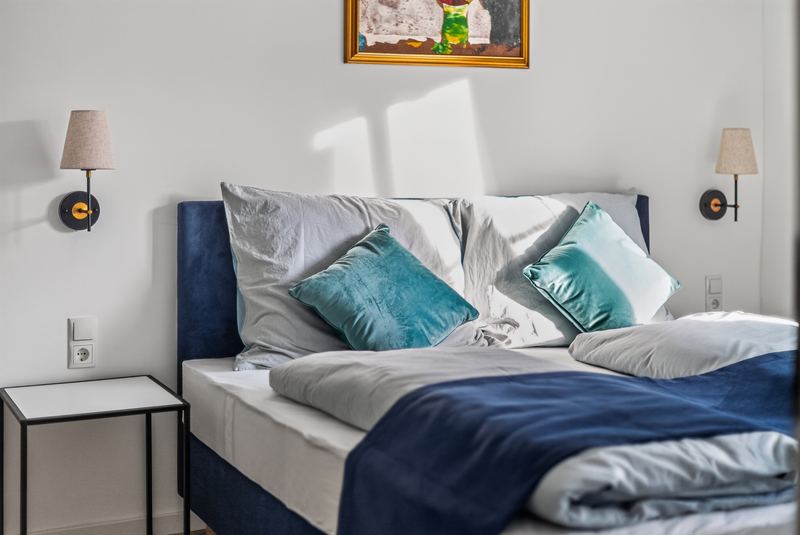 Top 6: close-up of the double bed with teal velvet cushions and two wall lamps